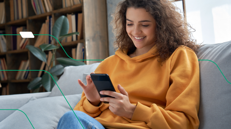 open finance vale a pena - mulher de jaqueta de moletom amarela sentada em um sofá, mexendo no celular e sorrindo
